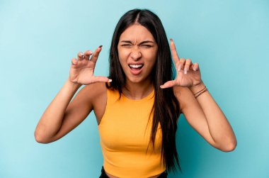 Mavi arka planda izole edilmiş genç İspanyol kadın pençelerini bir kediyi taklit ederken gösteriyor, agresif bir hareket..