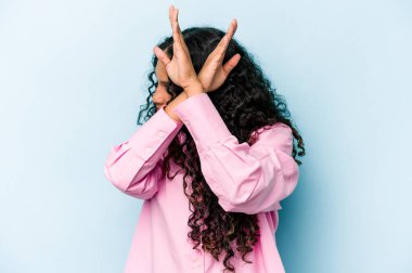 Mavi arka planda izole edilmiş genç İspanyol kadın iki kolu çapraz tutuyor, inkar kavramı.