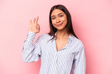 Pembe arka planda izole edilmiş genç İspanyol kadın bir göz kırptı ve elleriyle iyi bir jest yaptı..