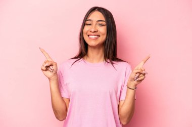 Pembe arka planda izole edilmiş genç İspanyol kadın iki parmağı da boş bir alan gösteriyor..