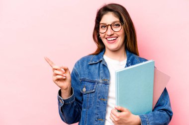 Pembe arka planda izole edilmiş genç beyaz kadın gülümsüyor ve boş alanda bir şeyler gösteriyor..