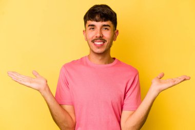 Sarı arka planda izole genç beyaz adam kollarıyla ölçek yapar, mutlu ve kendinden emin hisseder..