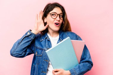 Pembe arka planda izole edilmiş genç beyaz kadın bir dedikoduyu dinlemeye çalışıyor..