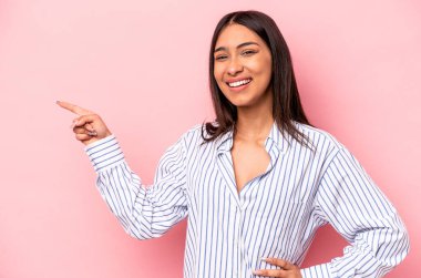 Pembe arka planda izole edilmiş genç İspanyol kadın işaret parmağıyla işaret ederek gülümsüyor..