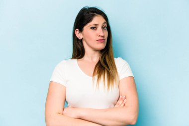 Mavi arka planda izole edilmiş genç beyaz kadın alaycı bir ifadeyle kameraya bakarken mutsuz oluyor..