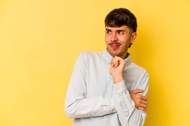 Sarı arka planda izole edilmiş genç beyaz adam şaşkın, şüpheli ve güvensiz hissediyor..