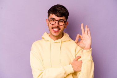 Mor arka planda izole edilmiş genç beyaz bir adam bir göz kırptı ve elleriyle iyi bir jest yaptı..