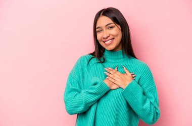 Pembe arka planda izole edilmiş genç İspanyol kadın, avuçlarını göğsüne bastıran dostça bir ifadeye sahiptir. Aşk konsepti.