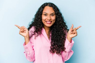 Mavi arka planda izole edilmiş genç İspanyol kadın farklı kopya alanlarını gösteriyor, birini seçiyor, parmaklarıyla gösteriyor..