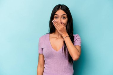 Mavi arka planda izole edilmiş genç İspanyol kadın şok olmuş, ağzı ellerle kaplanmış, yeni bir şey keşfetmeye hevesli..