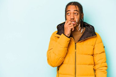 Genç Afrikalı Amerikalı bir adam mavi arka planda izole edilmiş rahat bir şekilde bir şeyin fotokopi odasına baktığını düşünüyor..