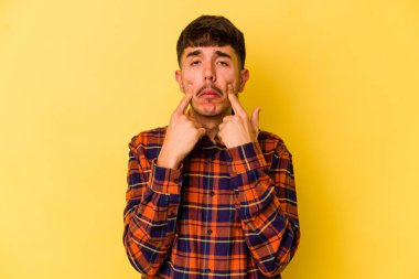 Kafkasyalı genç adam sarı arka planda izole edilmiş, ağlıyor, bir şeyden memnun değil, acı ve kafa karışıklığı kavramı..