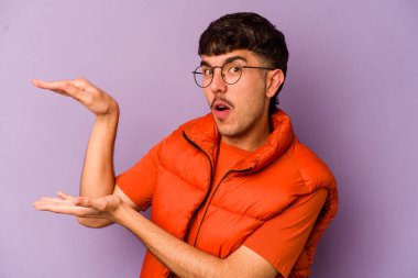 Mor arka planda izole genç beyaz adam iki eliyle bir şey tutuyor, ürün sunumu..