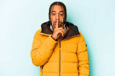 Genç Afrikalı Amerikalı bir adam mavi arka planda izole edilmiş bir şekilde sır saklıyor ya da sessizlik istiyor..