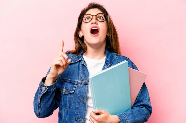 Pembe arka planda izole edilmiş genç beyaz kadın ağzı açık bir şekilde üst tarafı işaret ediyor..