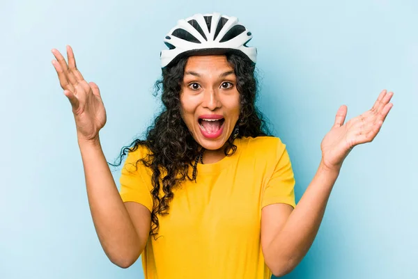 若いですヒスパニック女性身に着けていますヘルメット自転車青の背景に隔離された快適な驚きを受けます 興奮し 手を上げます — ストック写真