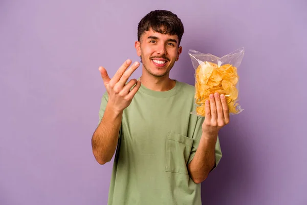 Jonge Spaanse Man Met Chips Geïsoleerd Paarse Achtergrond Wijzend Met — Stockfoto