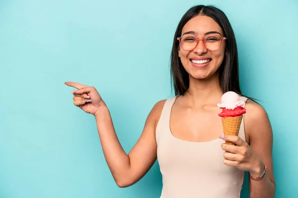年轻的惊慌失措的女人拿着一个蓝色背景的冰淇淋 微笑着指着旁边 在空旷的空间里展示着一些东西 — 图库照片
