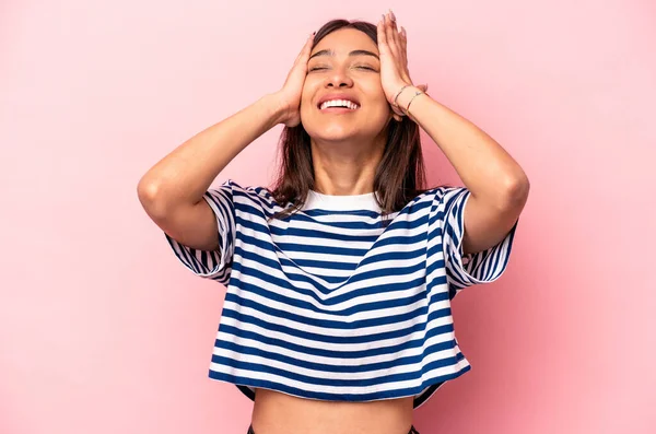 Pembe arka planda izole edilmiş genç İspanyol kadın mutlu bir şekilde ellerini başının üstünde tutuyor. Mutluluk kavramı.