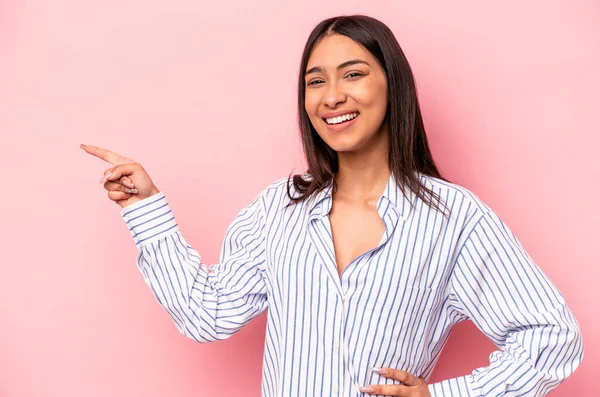 Pembe arka planda izole edilmiş genç İspanyol kadın işaret parmağıyla işaret ederek gülümsüyor..