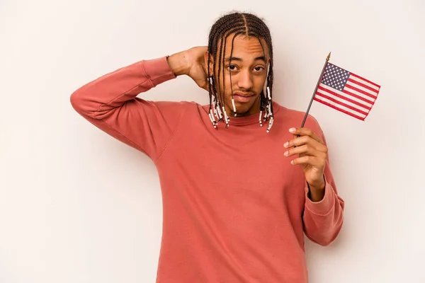 アフリカ系アメリカ人の若い男は 頭の後ろに触れ 選択をする白い背景に隔離されたアメリカの旗を持っている — ストック写真