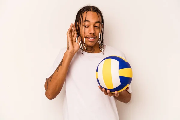 Young African American man playing volleyball isolated on white background trying to listening a gossip.