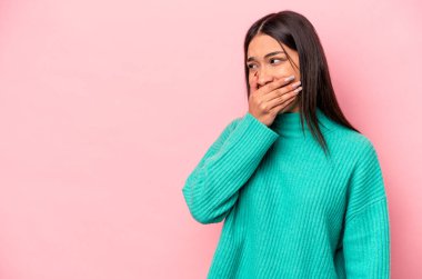 Genç İspanyol kadın pembe arka planda izole edilmiş. Düşünceli bir şekilde bir fotokopi odasına bakıyor. Ağzını eliyle kapatıyor..