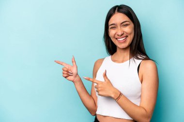 Mavi arka planda izole edilmiş genç İspanyol kadın işaret parmaklarıyla işaret ederek heyecanlanıyor..