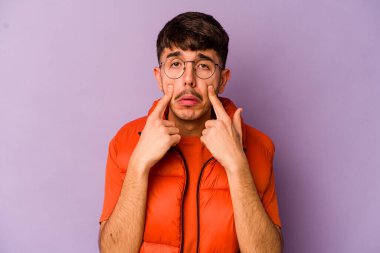 Mor arka planda izole edilmiş genç beyaz bir adam ağlıyor, bir şeyden memnun değil, acı ve kafa karışıklığı konsepti..