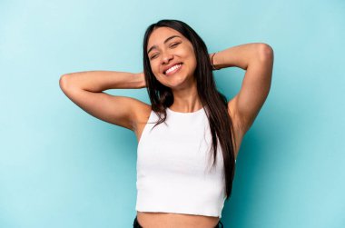 Mavi arka planda izole edilmiş genç İspanyol kadın kollarını uzatıyor, rahat pozisyonda..