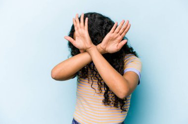 Mavi arka planda izole edilmiş genç İspanyol kadın iki kolu çapraz tutuyor, inkar kavramı.