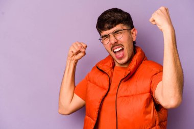 Mor arka planda izole edilmiş genç beyaz adam zafer kazandıktan sonra yumruğunu kaldırıyor, kazanan konsept..