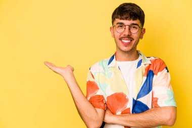Sarı arka planda izole edilmiş genç beyaz bir adam bir palmiye üzerinde fotokopi alanı gösteriyor ve belinde başka bir el tutuyor..