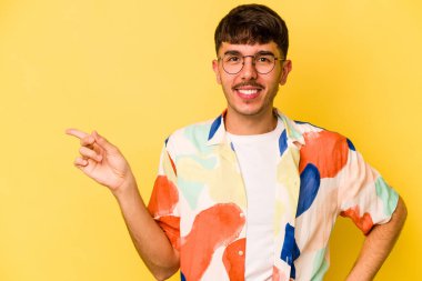 Sarı arka planda izole edilmiş genç beyaz adam işaret parmağıyla işaret ederek gülümsüyor..