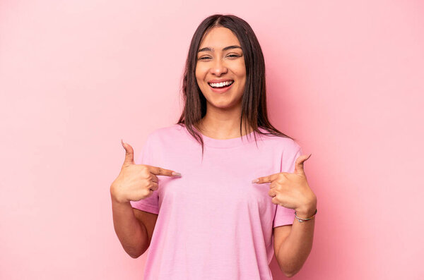 Young hispanic woman isolated on pink background surprised pointing with finger, smiling broadly.