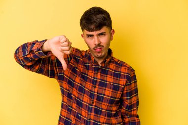 Sarı arka planda izole edilmiş genç beyaz adam baş parmağını aşağı gösteriyor ve hoşlanmadığını ifade ediyor..