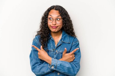 Beyaz arka planda izole edilmiş genç İspanyol kadın iki seçenek arasında seçim yapmaya çalışıyor..