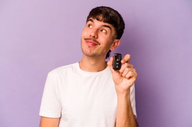 Mor arka planda izole edilmiş anahtar taşıyan İspanyol genç adam hedeflerine ve amaçlarına ulaşma hayali kuruyor.