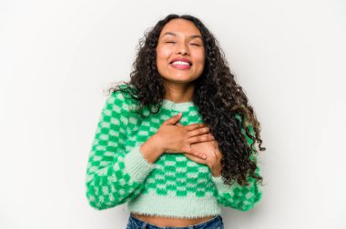 Beyaz arka planda izole edilmiş genç İspanyol kadın gülüyor, ellerini kalbe koyuyor, mutluluk kavramını koruyor..