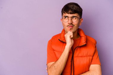Mor arka planda izole edilmiş genç beyaz adam şüpheli ve şüpheci bir ifadeyle yana bakıyor..