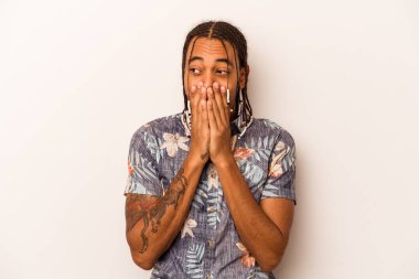 Genç Afro-Amerikalı bir adam beyaz arka planda izole edilmiş bir şekilde bir şeylere gülüyor, elleriyle ağzını kapatıyor..