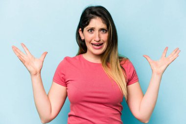 Mavi arka planda izole edilmiş genç beyaz kadın gökyüzüne haykırıyor, yukarı bakıyor, hayal kırıklığına uğramış..