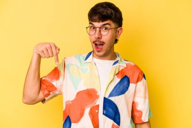 Sarı arka planda izole edilmiş genç beyaz bir adam gömlek fotokopi alanını elle gösteriyor, gururlu ve kendinden emin.