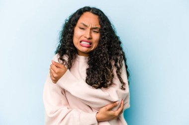 Genç İspanyol kadın mavi arka planda izole edilmiş, dirsek masajı yapıyor, kötü bir hareketin ardından acı çekiyor..