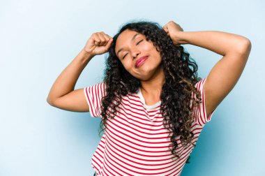 Mavi arka planda izole edilmiş genç İspanyol kadın kollarını uzatıyor, rahat pozisyonda..