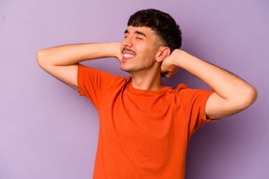 Mor arka planda izole olmuş genç beyaz bir adam kendini güvende hissediyor, elleri başının arkasında..