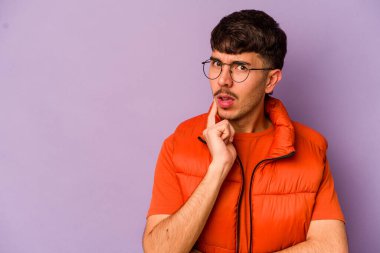Mor arka planda izole edilmiş genç beyaz adam şüpheli ve şüpheci bir ifadeyle yana bakıyor..