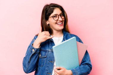 Pembe arka planda izole edilmiş genç bir beyaz kadın cep telefonu hareketini parmaklarıyla gösteriyor..