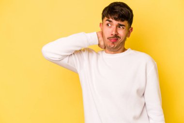 Kafkasyalı genç adam sarı arka planda izole edilmiş kafasının arkasına dokunuyor, düşünüyor ve bir seçim yapıyor..