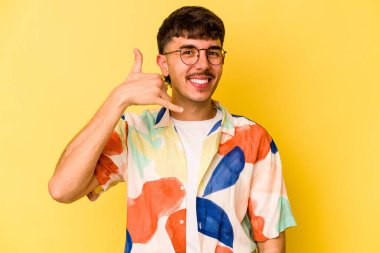 Sarı arka planda izole edilmiş genç beyaz adam parmaklarıyla bir cep telefonu hareketi gösteriyor..